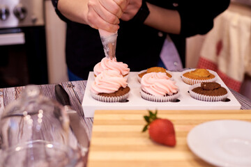 Female hands fill cupcakes with soft cream close-up.