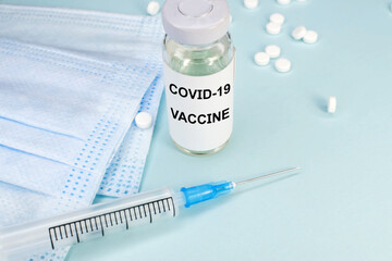 A vaccine against coronavirus. An ampoule and a syringe near a medical mask and tablets. Medical concept.
