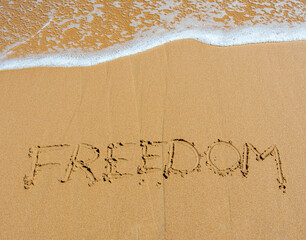 freedom written in sand at beach with wave