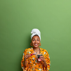 Vertical shot of happy dark skinned Afro American woman eats cold ice cream enjoys spending time at...