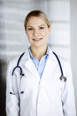 Friendly female doctor standing in clinic. Portrait of cheerful smiling physician. Perfect medical service in hospital. Medicine and healthcare concept