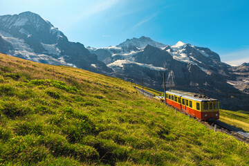 Fototapeta na wymiar Electric retro tourist train and snowy mountains in background, Switzerland