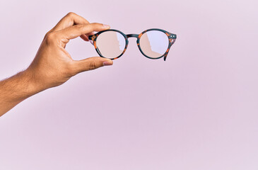 Hand of hispanic man holding glasses over isolated pink background.
