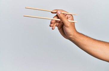 Hand of hispanic man holding wooden chopsticks over isolated white background.
