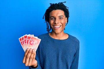 Young african american man holding 20 israel shekels banknotes looking positive and happy standing and smiling with a confident smile showing teeth