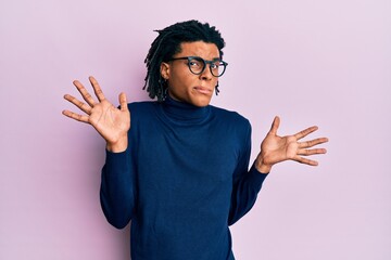 Young african american man wearing turtleneck sweater and glasses clueless and confused with open...