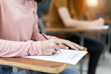 Close up of young female university students concentrate on doing examination in the classroom. Girl student writes the answer of the examinations on answer sheet in the classroom.