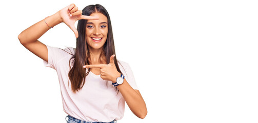 Young hispanic woman wearing casual white tshirt smiling making frame with hands and fingers with happy face. creativity and photography concept.
