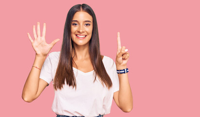 Young hispanic woman wearing casual white tshirt showing and pointing up with fingers number six while smiling confident and happy.