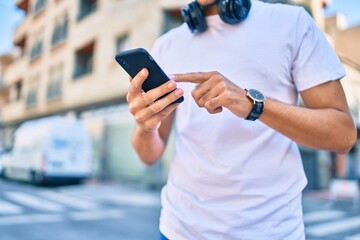 Young latin man using smartphone and headphones at the city.