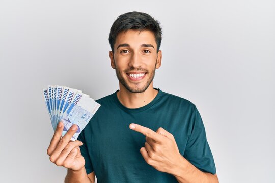 Young handsome man holding 1000 south korean won banknotes smiling happy pointing with hand and finger