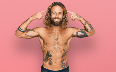 Fototapeta premium Handsome man with beard and long hair standing shirtless showing tattoos smiling pointing to head with both hands finger, great idea or thought, good memory