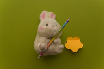 White toy fluffy rabbit with holding a pencil for writing on a green background