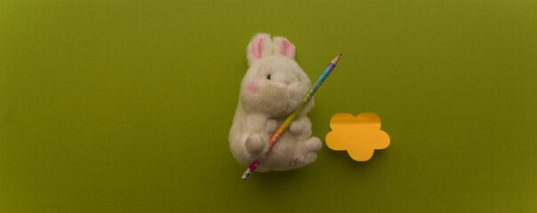 White toy fluffy rabbit with holding a pencil for writing on a green background