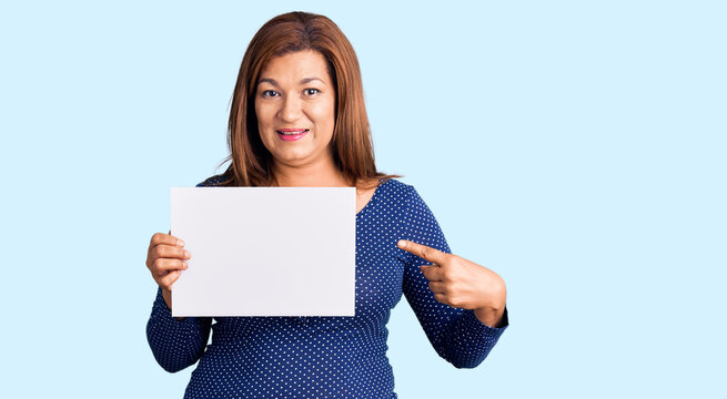 Middle age latin woman holding paper banner with blank space smiling happy pointing with hand and finger