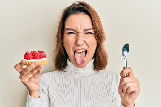 Young caucasian woman holding sweet pastry sticking tongue out happy with funny expression.