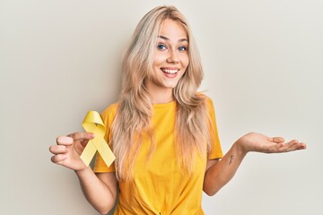 Beautiful caucasian blonde girl holding suicide prevention yellow ribbon celebrating achievement with happy smile and winner expression with raised hand