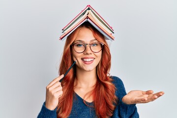 Young redhead woman holding books over head celebrating achievement with happy smile and winner...