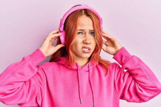 Young redhead woman listening to music using headphones clueless and confused expression. doubt concept.