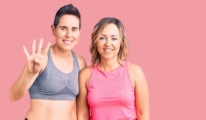 Couple of women wearing sportswear showing and pointing up with fingers number four while smiling confident and happy.