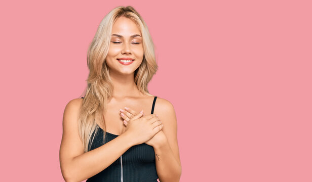 Young blonde girl wearing elegant and sexy look smiling with hands on chest with closed eyes and grateful gesture on face. health concept.