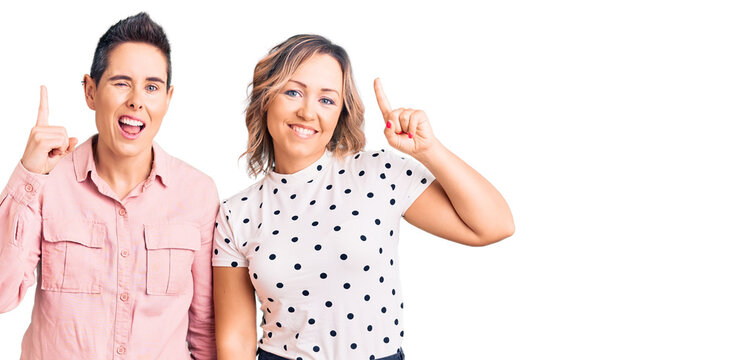 Couple of women wearing casual clothes pointing finger up with successful idea. exited and happy. number one.