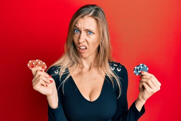 Beautiful caucasian woman playing poker holding casino chips in shock face, looking skeptical and...