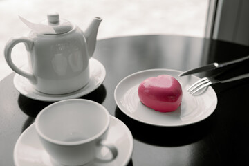 cake in heart shape. Red cupcake in the shape of a heart on a dark gray background. Valentine's Day. Dessert on a plate with a cup of tea and a teapot.