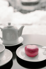 cake in heart shape. Red cupcake in the shape of a heart on a dark gray background. Valentine's Day. Dessert on a plate with a cup of tea and a teapot.