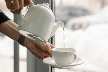 Woman pours black tea into a cup in a cafe. Steam and drops from aromatic and hot tea.