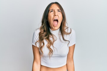 Young brunette woman wearing casual white t shirt angry and mad screaming frustrated and furious,...