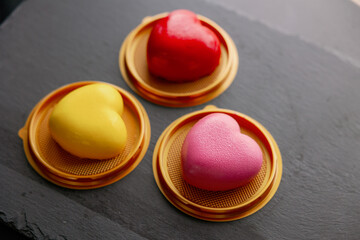 Composition of three mousse cakes in the shape of a heart. Desserts and gifts for Valentine's Day and February 14th. Pink, yellow and red glaze colors. Black background