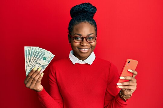 Young african american woman using smartphone holding usa dollars smiling with a happy and cool smile on face. showing teeth.