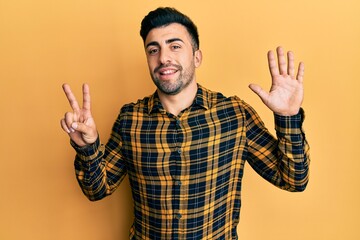 Naklejka premium Young hispanic man wearing casual clothes showing and pointing up with fingers number seven while smiling confident and happy.