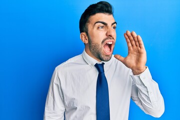 Young hispanic man wearing business clothes shouting and screaming loud to side with hand on mouth. communication concept.