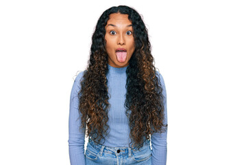 Young hispanic woman with curly hair wearing casual clothes sticking tongue out happy with funny expression. emotion concept.