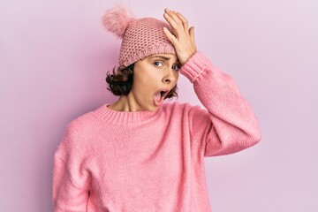 Young brunette woman wearing cute wool cap surprised with hand on head for mistake, remember error....