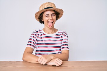 Young hispanic woman wearing casual clothes and hat sitting on the table winking looking at the...