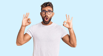 Naklejka premium Young hispanic man wearing casual clothes and glasses looking surprised and shocked doing ok approval symbol with fingers. crazy expression