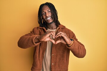 African american man with braids wearing brown retro jacket smiling in love doing heart symbol...