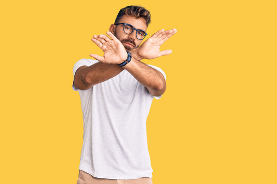 Young hispanic man wearing casual clothes and glasses rejection expression crossing arms and palms doing negative sign, angry face