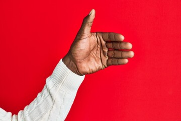 Arm and hand of african american black young man over red isolated background holding invisible object, empty hand doing clipping and grabbing gesture
