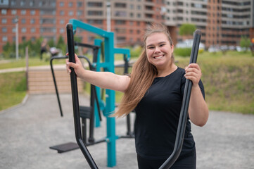 Beautiful smiling overweight young woman does fitness on an ellipsoid simulator outdoors. Fat girl...