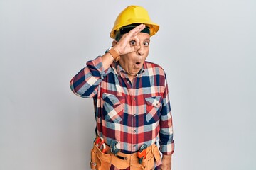Senior hispanic man wearing handyman uniform doing ok gesture shocked with surprised face, eye looking through fingers. unbelieving expression.