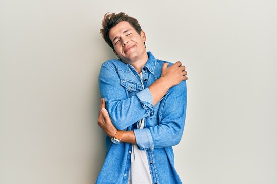 Handsome caucasian man wearing casual denim jacket hugging oneself happy and positive, smiling confident. self love and self care