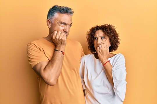 Beautiful middle age couple together wearing casual clothes looking stressed and nervous with hands on mouth biting nails. anxiety problem.