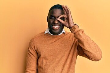 Young african american man wearing casual clothes doing ok gesture with hand smiling, eye looking through fingers with happy face.