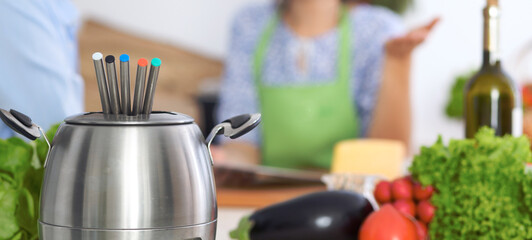 Fondue in a pot at the background of friends cooking together, close-up. Kitchen interiors and cookware