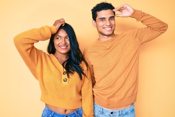 Beautiful latin young couple wearing casual clothes together smiling confident touching hair with hand up gesture, posing attractive and fashionable