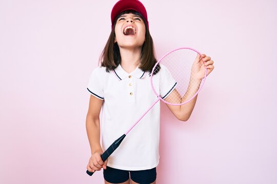 Young little girl with bang holding badminton racket angry and mad screaming frustrated and furious, shouting with anger looking up.